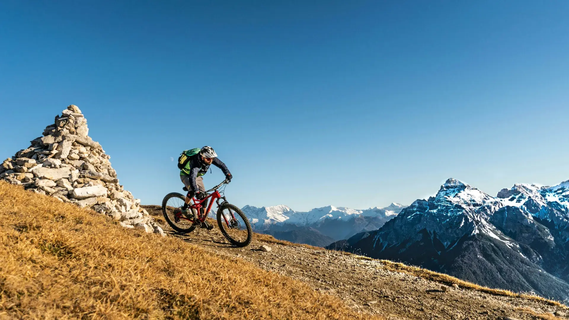 Mountainbiker zieht mit Schräglage durch einen Anlieger auf einem Flow Trail hoch über einem Alpental