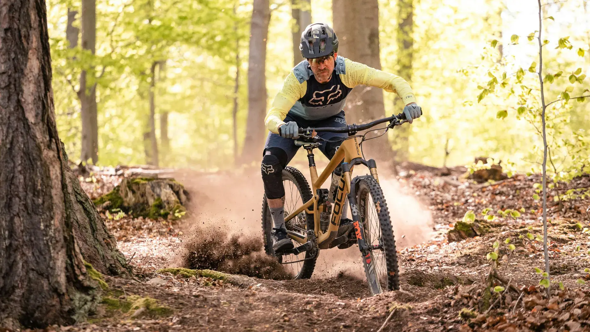 Einsteiger fährt eine breite blaue Flowline mit Anliegern in einem Alpen-Bikepark, Familie mit Kindern im Hintergrund am Übungsareal
